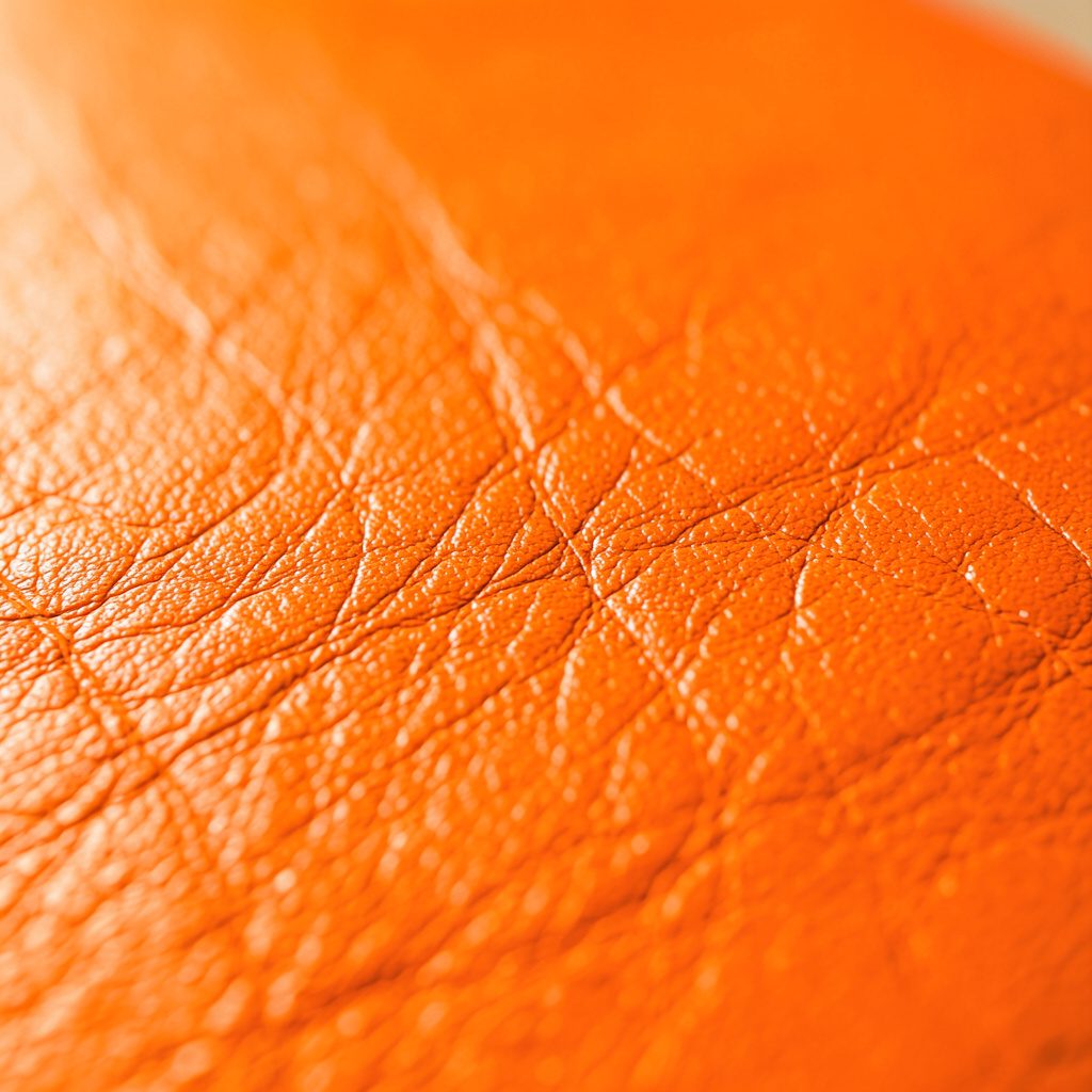 Extreme close-up photograph of handcrafted Italian leather in a warm tan tone, showing fine grain texture and a subtle sheen under soft directional light.