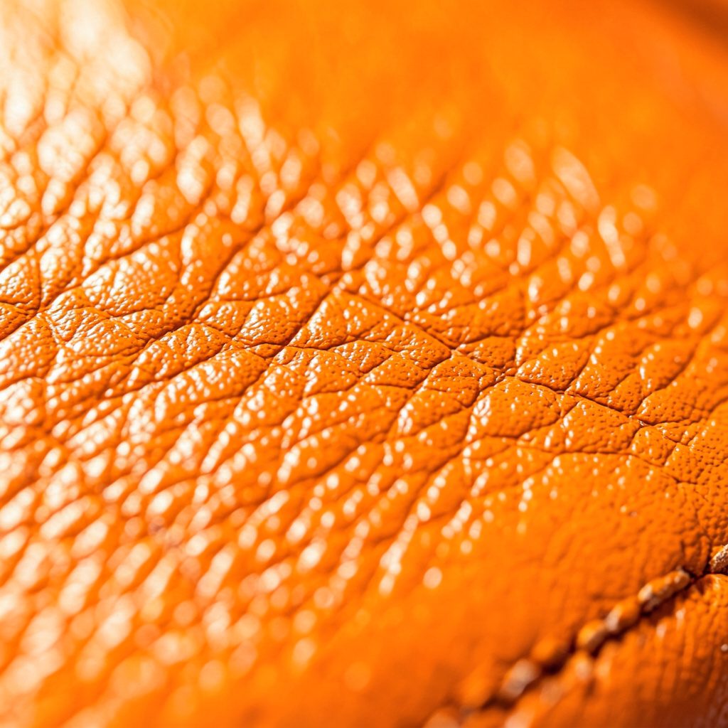 Extreme close-up of rich tan Italian leather strap texture against a polished gold watch case, warm brown and gold tones
