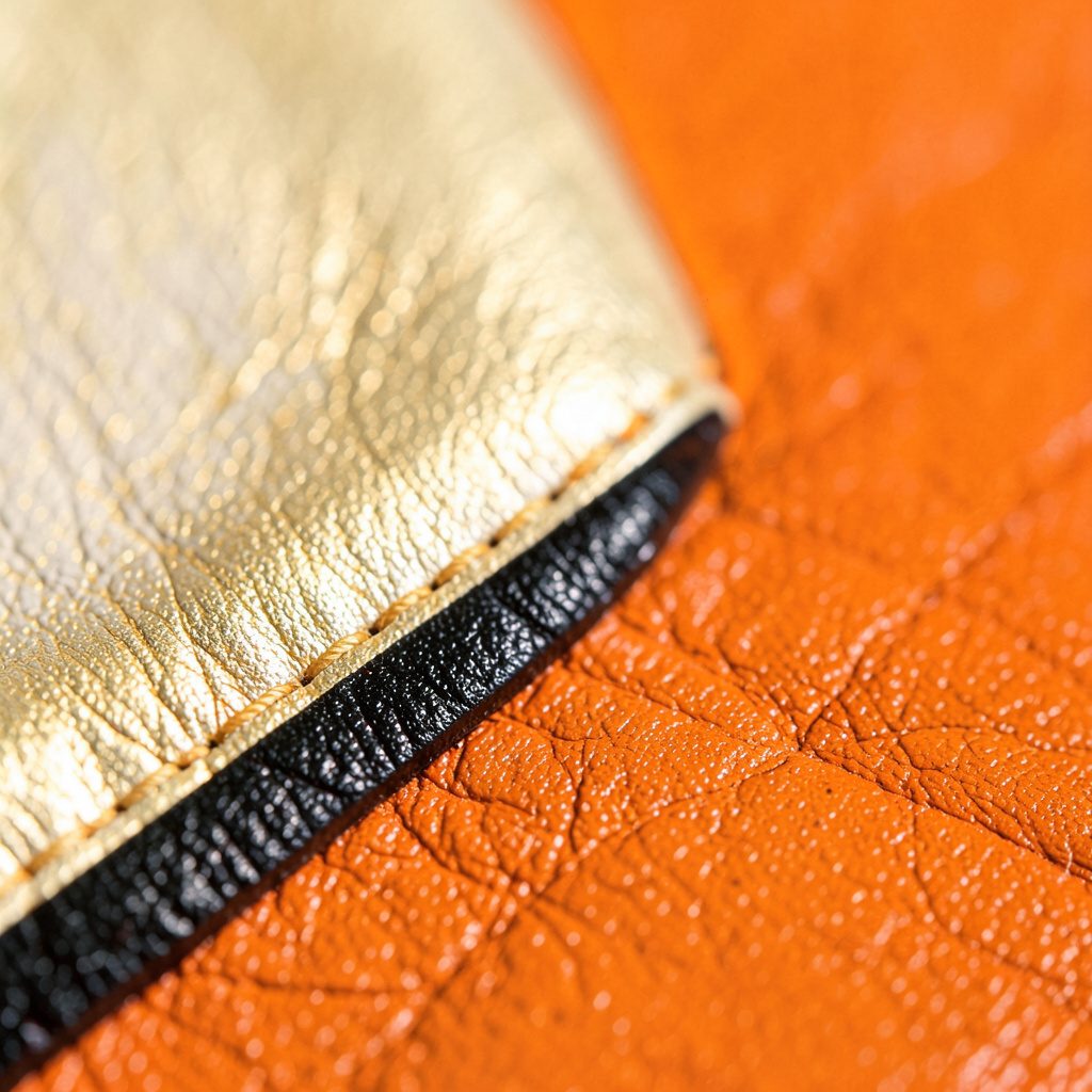 A sleek watch with a gold-tone case and black leather strap, photographed in dramatic side lighting on a dark surface.